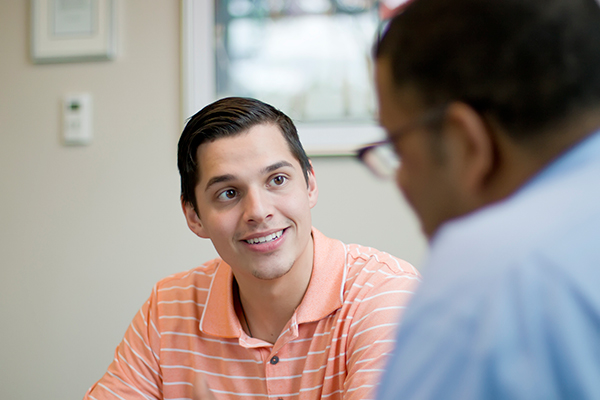 Male student in an orange shirt speaking with a counselor or adviser
